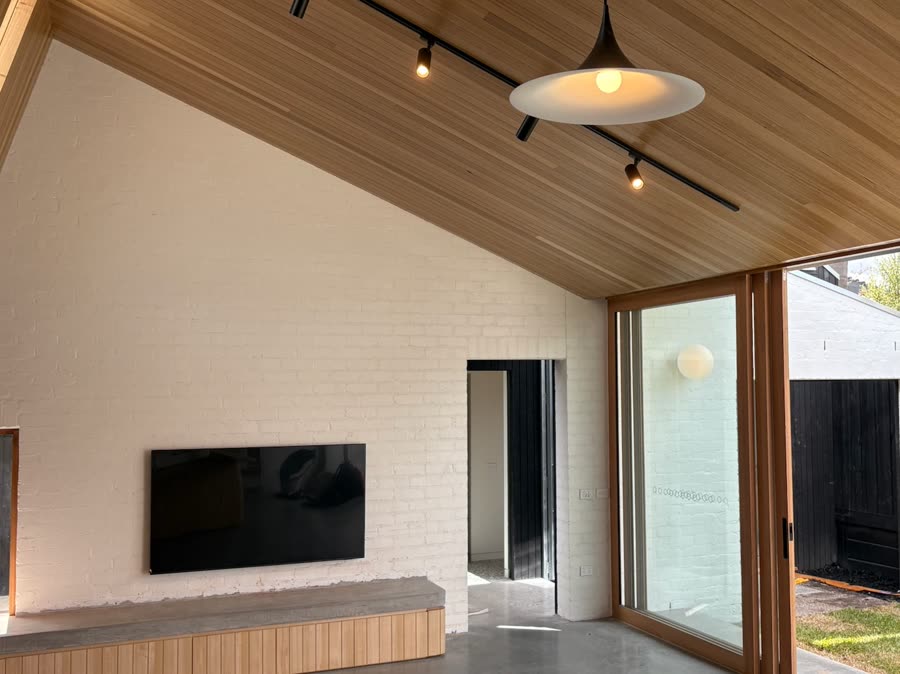A wall-mounted television on a white brick wall with no visible cabling, under a vaulted timber ceiling