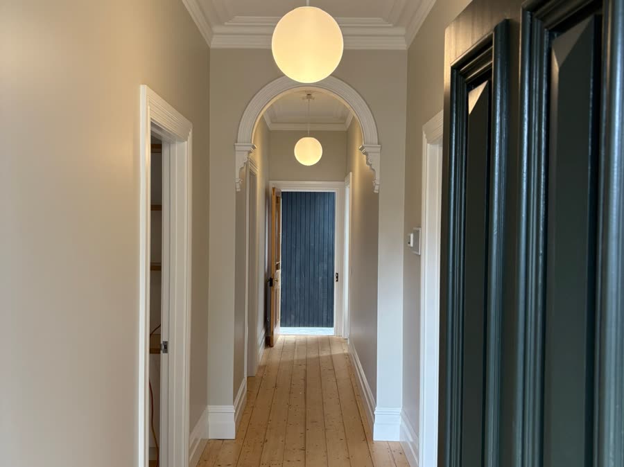 A period hallway running through an arch, with ceiling roses and two globe pendants