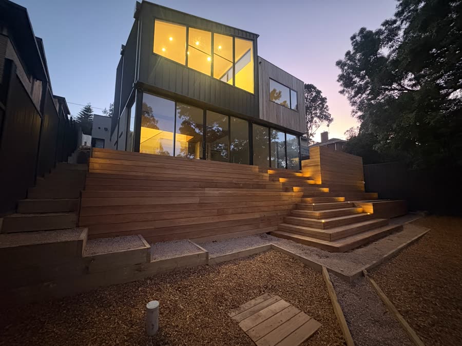 A two-storey extension lit at dusk, with step lights running up a timber deck