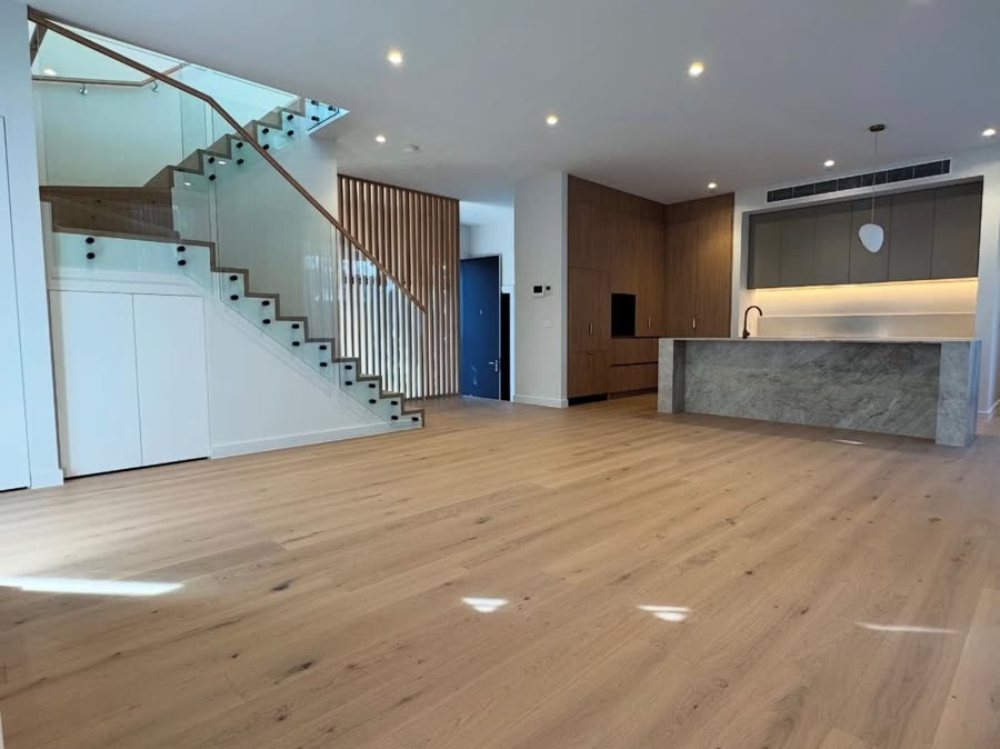 An empty open-plan living space in a new build, with a glass balustrade stair and recessed downlights