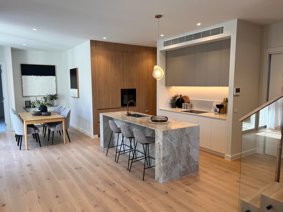 A renovated kitchen with a stone island bench, timber joinery and a pendant over the bench
