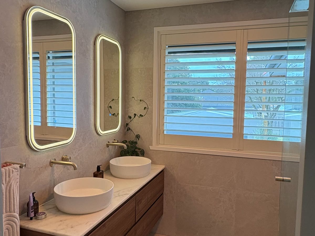 Bathroom with two backlit LED mirrors above a double vanity and a heat lamp fitted in the ceiling