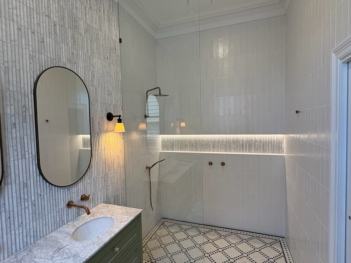 Bathroom with brass wall lights either side of the mirror and a lit shower niche