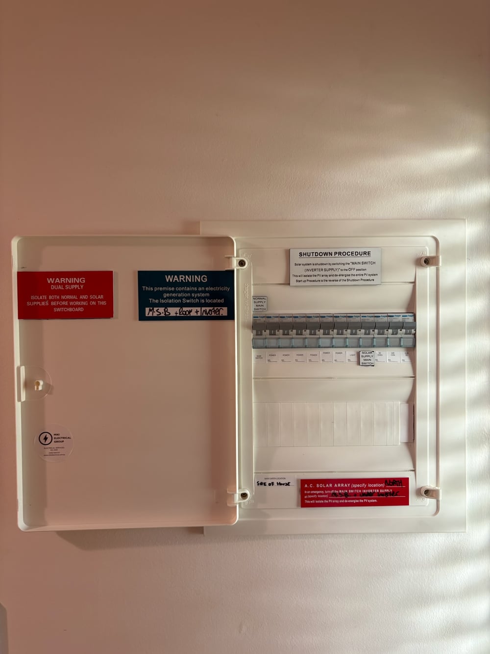 Open switchboard with solar supply, circuit breakers and dual-supply warning labels