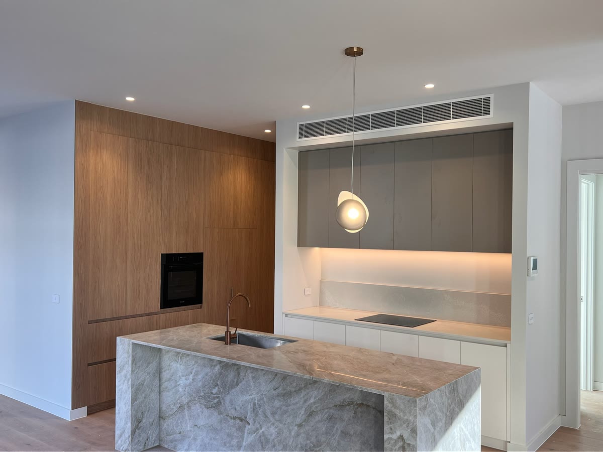 Kitchen with a stone island bench, timber joinery and a sculptural pendant over the sink