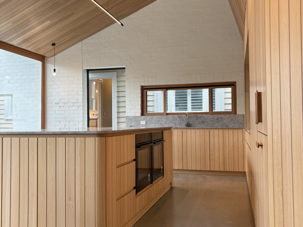 Timber-lined kitchen under a vaulted ceiling with a slimline linear pendant and recessed downlights