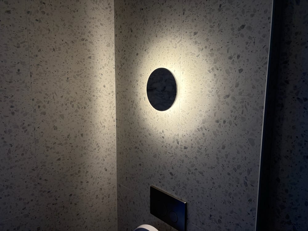 Round backlit LED wall sconce casting a warm halo on a terrazzo tiled wall